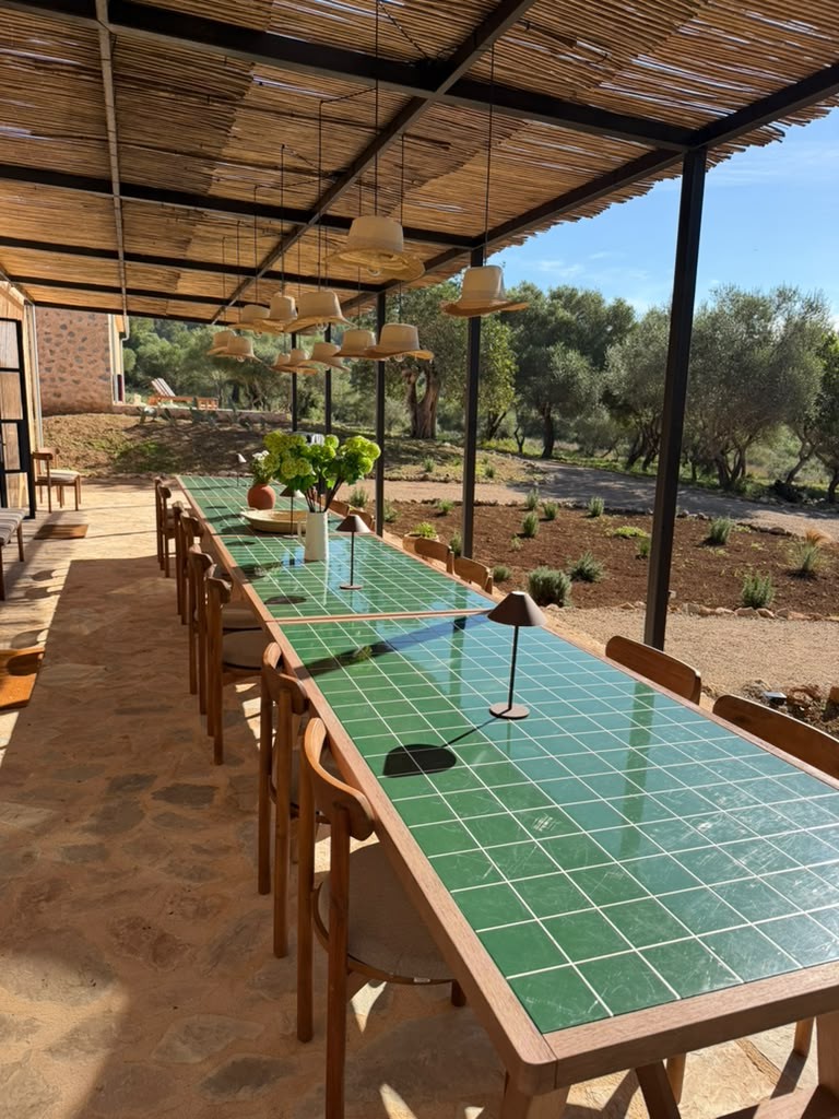 La larga mesa de azulejos verdes bajo la pérgola de cañizo, frente al olivar