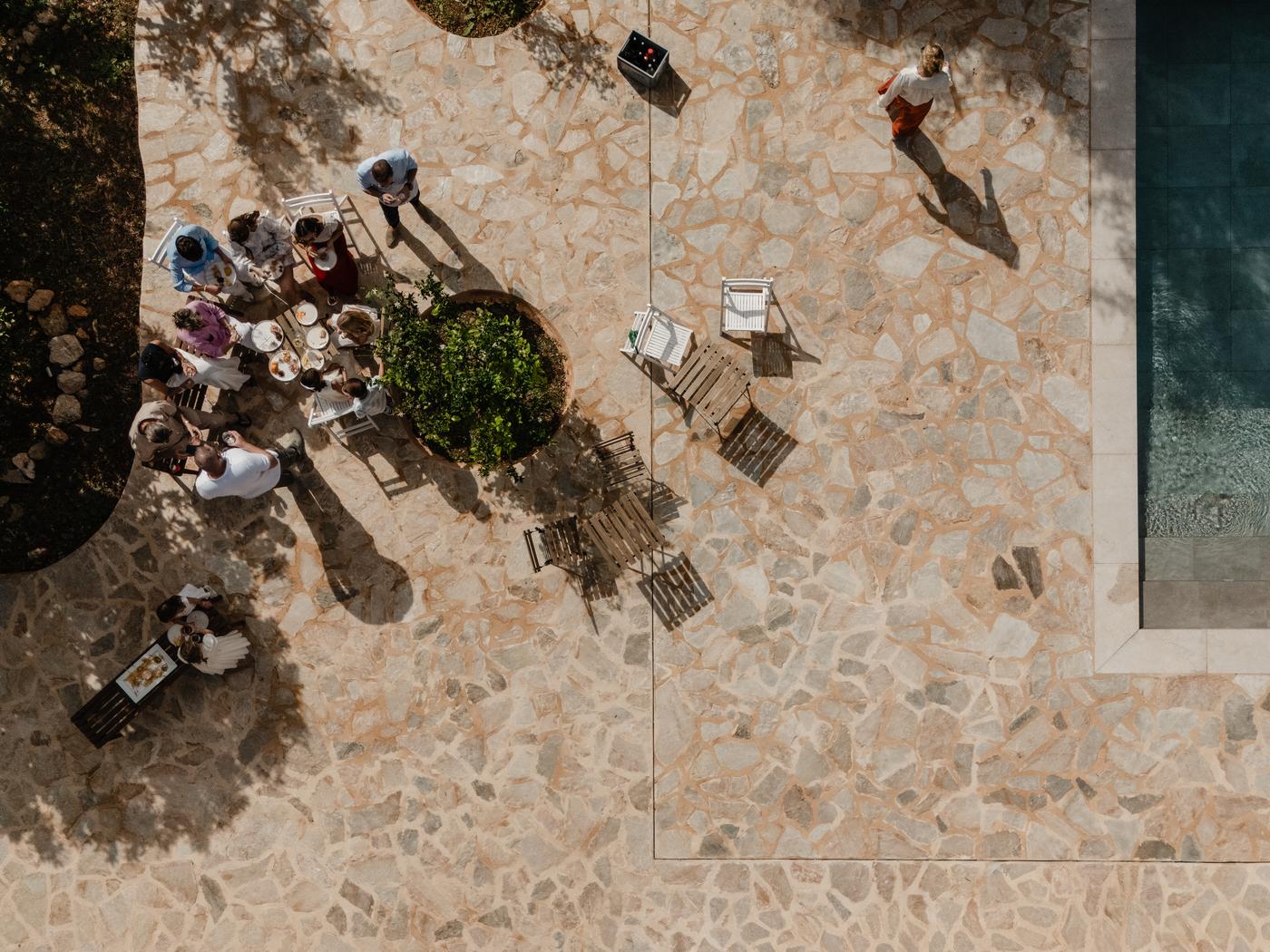 Invitados reunidos alrededor de una mesa junto a la piscina, vistos desde arriba