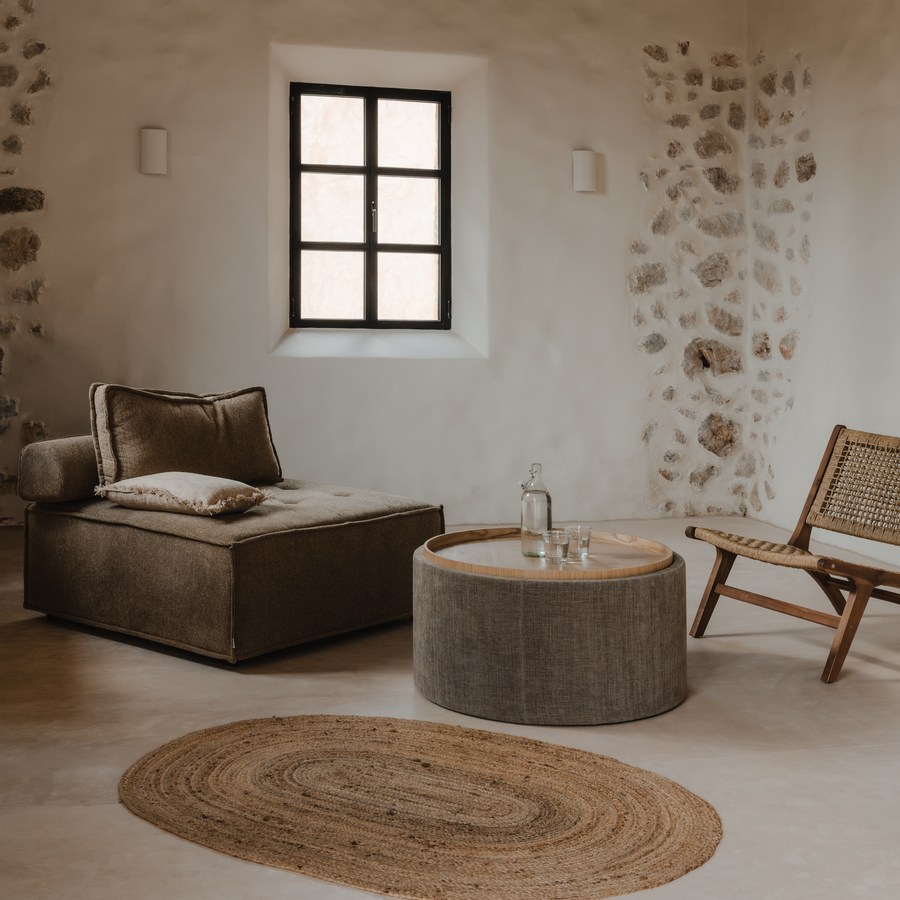 Salón de TERRA con muros de piedra vista, viga de madera y una alfombra de yute
