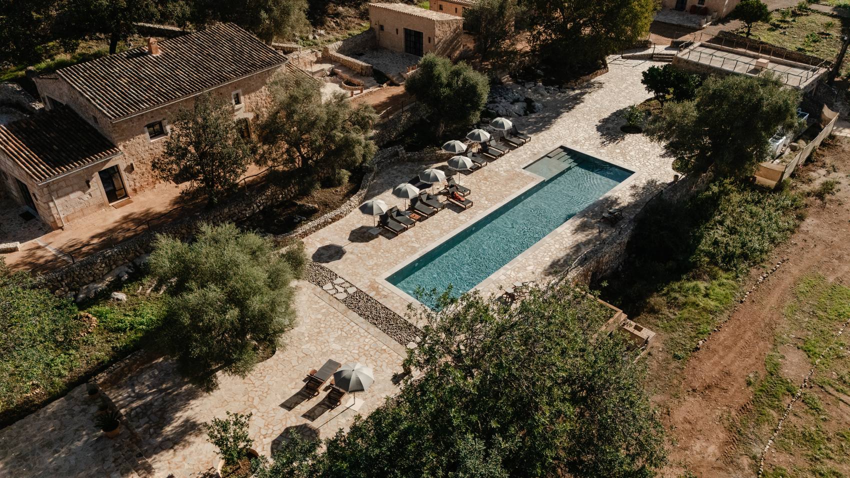Vista aérea de la piscina de TERRA, su terraza con sombrillas y las casas de piedra